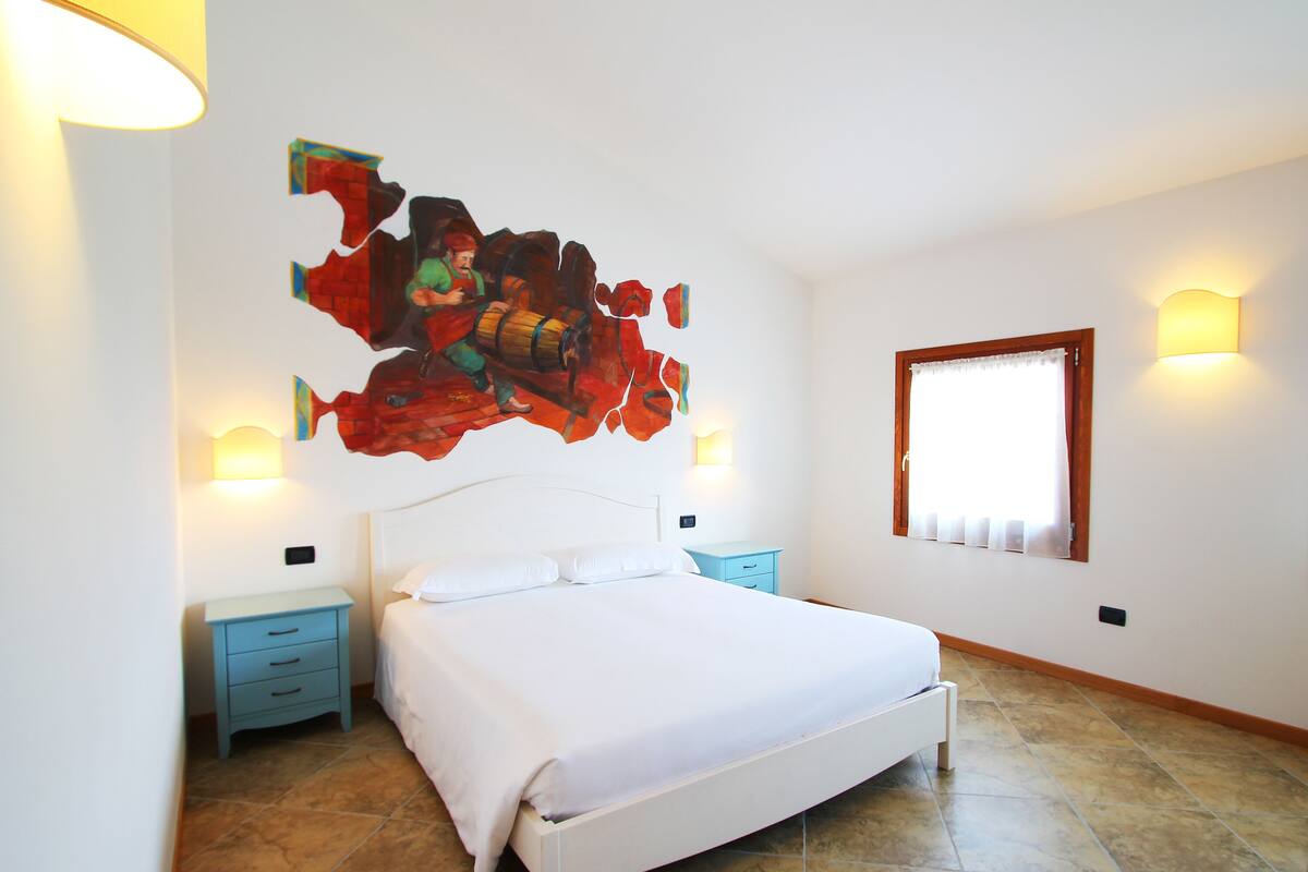 A bedroom with a white bed, two nightstands, a large abstract painting on the wall, and a window with curtains.