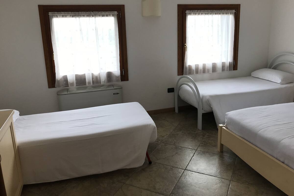 A room with two single beds, a radiator, and two windows with curtains.