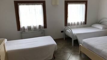 Quarto com duas camas de solteiro, um radiador e duas janelas com cortinas.