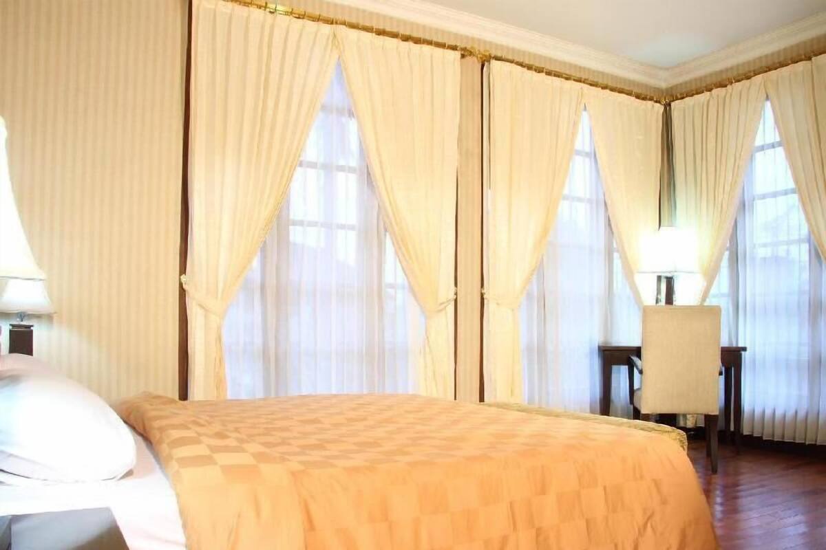 A hotel room with a bed, a chair, a desk, and curtains.