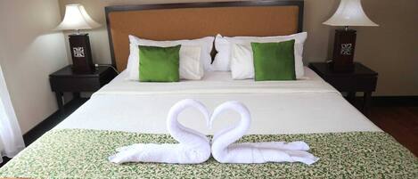 A neatly made bed with a green and white patterned bedspread, two white pillows, and a decorative swan towel arrangement.