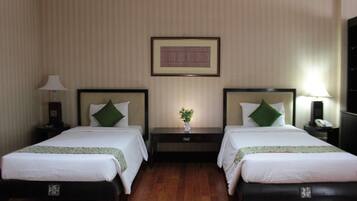 A hotel room with two single beds, a nightstand with a lamp, a small table with a vase, and a framed picture on the wall.