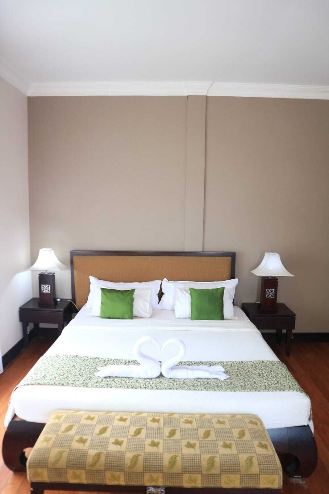 A hotel room with a large bed, two bedside tables, a nightstand, and a bench.