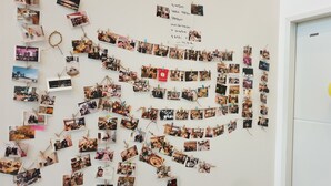 A wall covered with numerous photographs, some clipped with clothespins, and a few with handwritten notes. - Sol Guest House Haeundae (Busan)