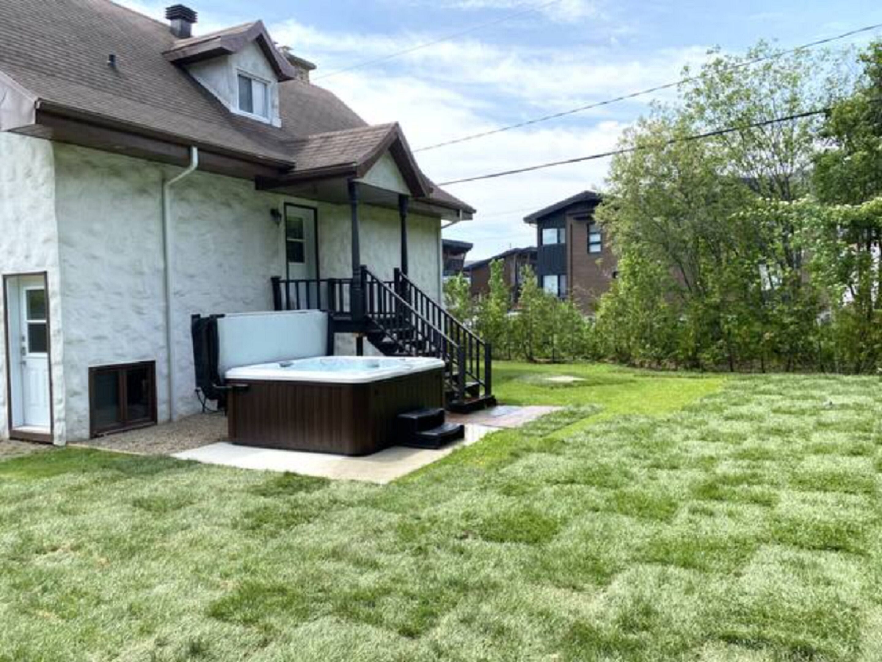 Une maison d’habitation avec un jacuzzi dans le jardin, un escalier menant au porche et une pelouse bien entretenue.