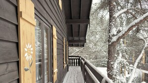 Un edificio de madera con balcón, árboles cubiertos de nieve y baranda de madera.