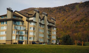 Un hotel de varios pisos con balcones, un estacionamiento y montañas al fondo.