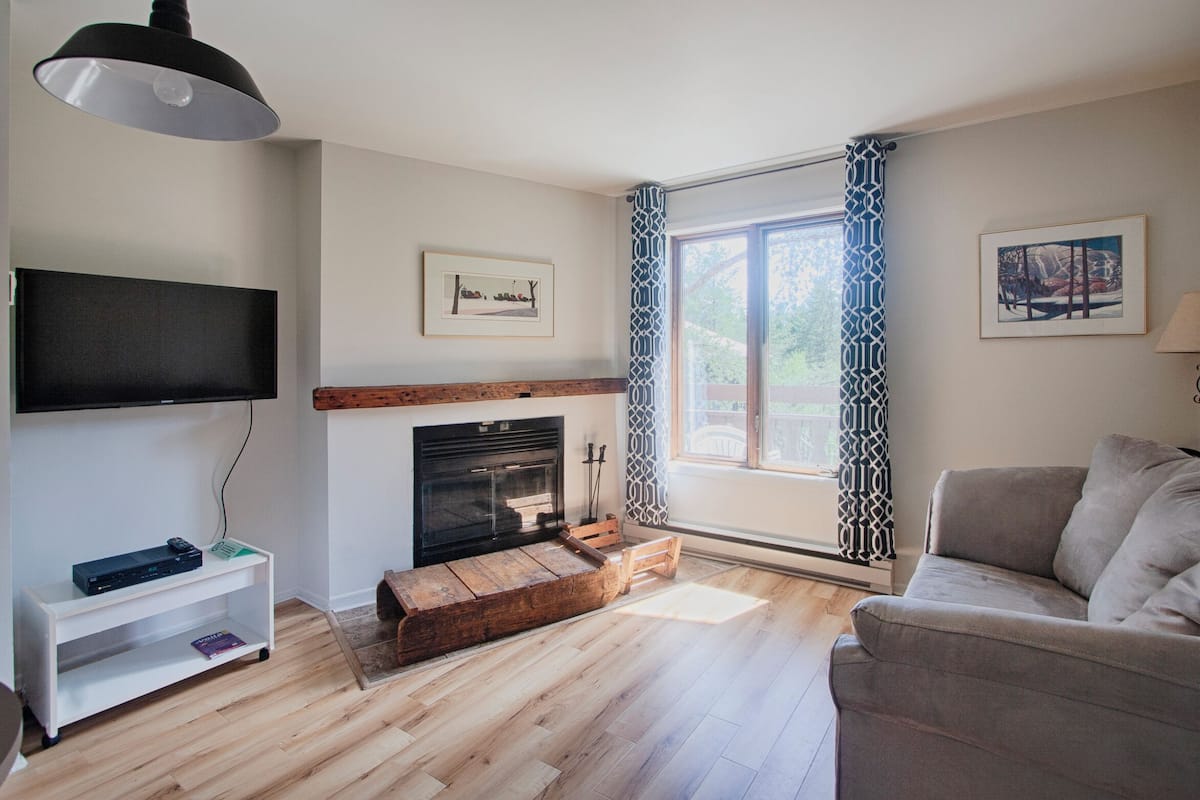 A living room with a fireplace, a sofa, a TV, and a window with patterned curtains.