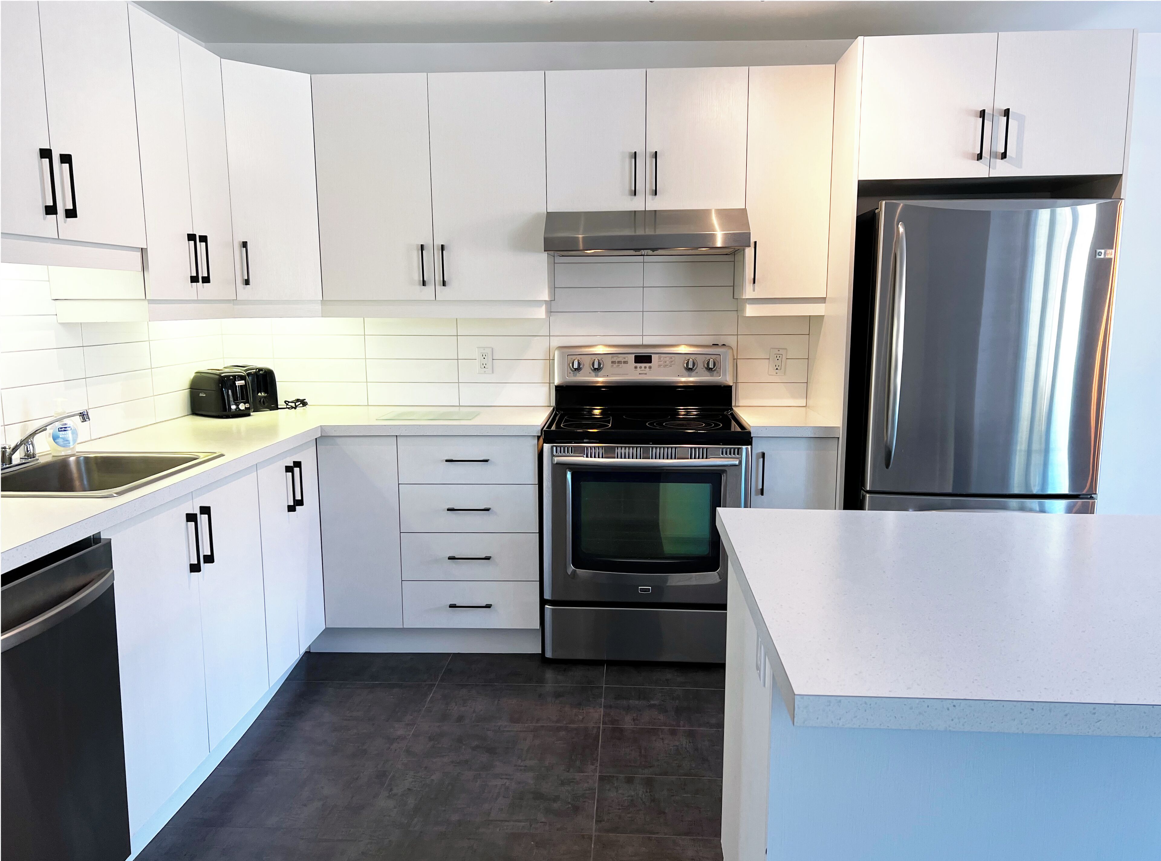 A modern kitchen with white cabinets, a stainless steel refrigerator, a built-in oven, and a gas stove.
