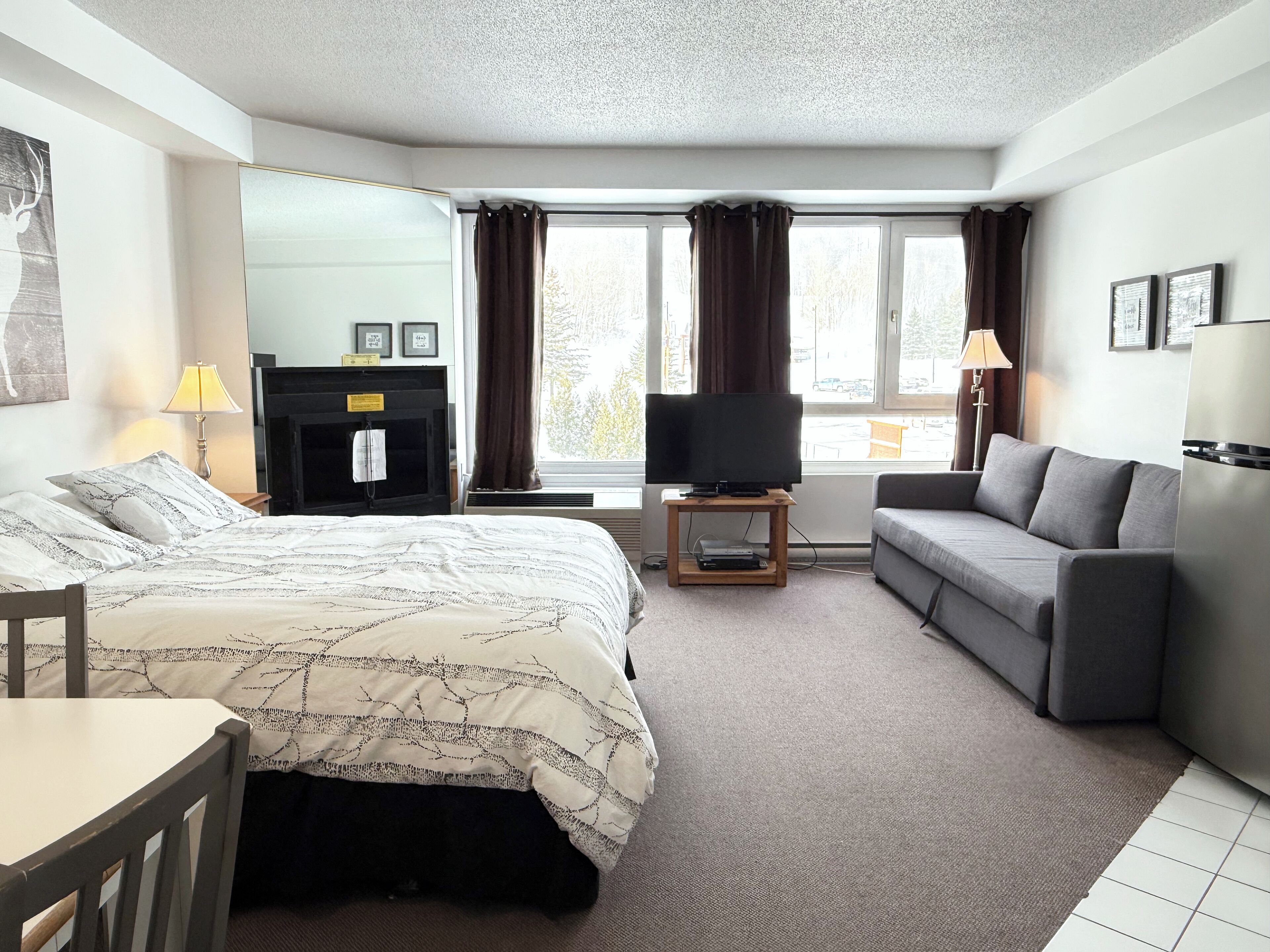 A hotel room with a bed, a sofa, a TV on a stand, a desk, and a chair.
