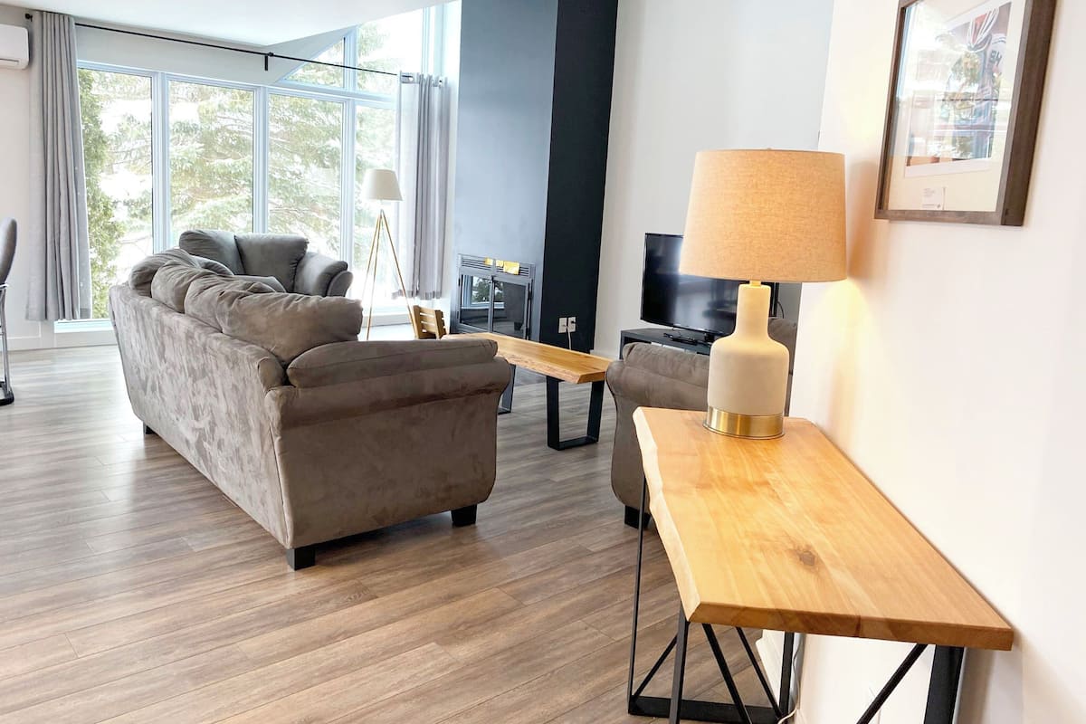 A modern living room with a sofa, a wooden side table, a lamp, and a television.