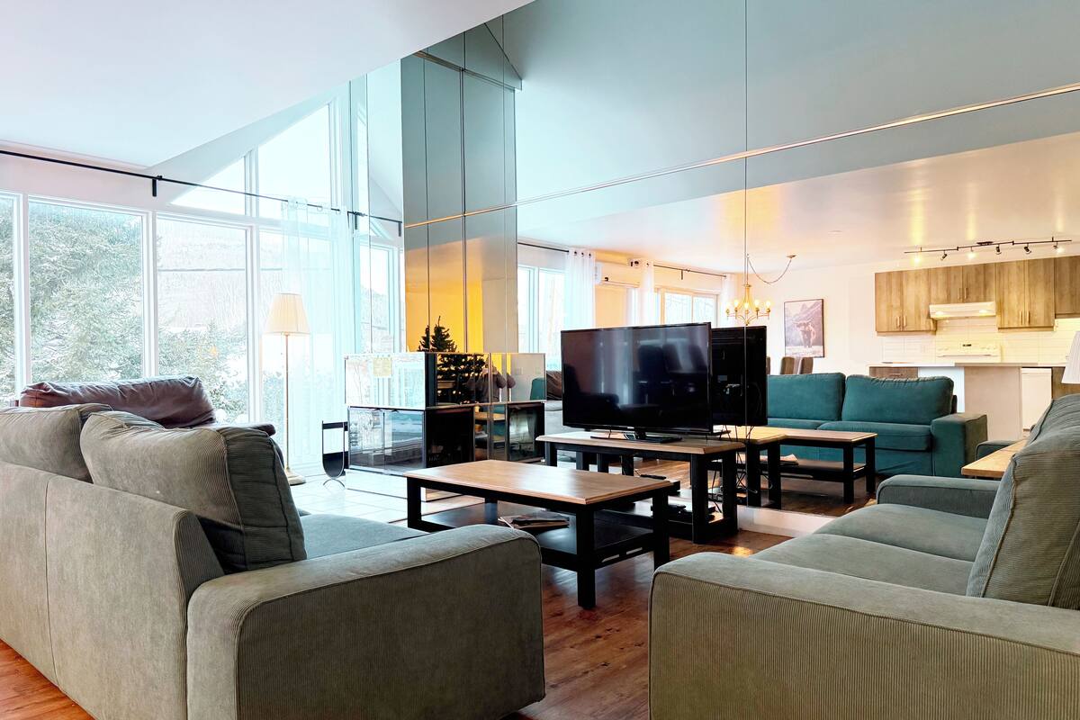 A modern living room with large windows, a flat-screen TV, and a cozy seating area.