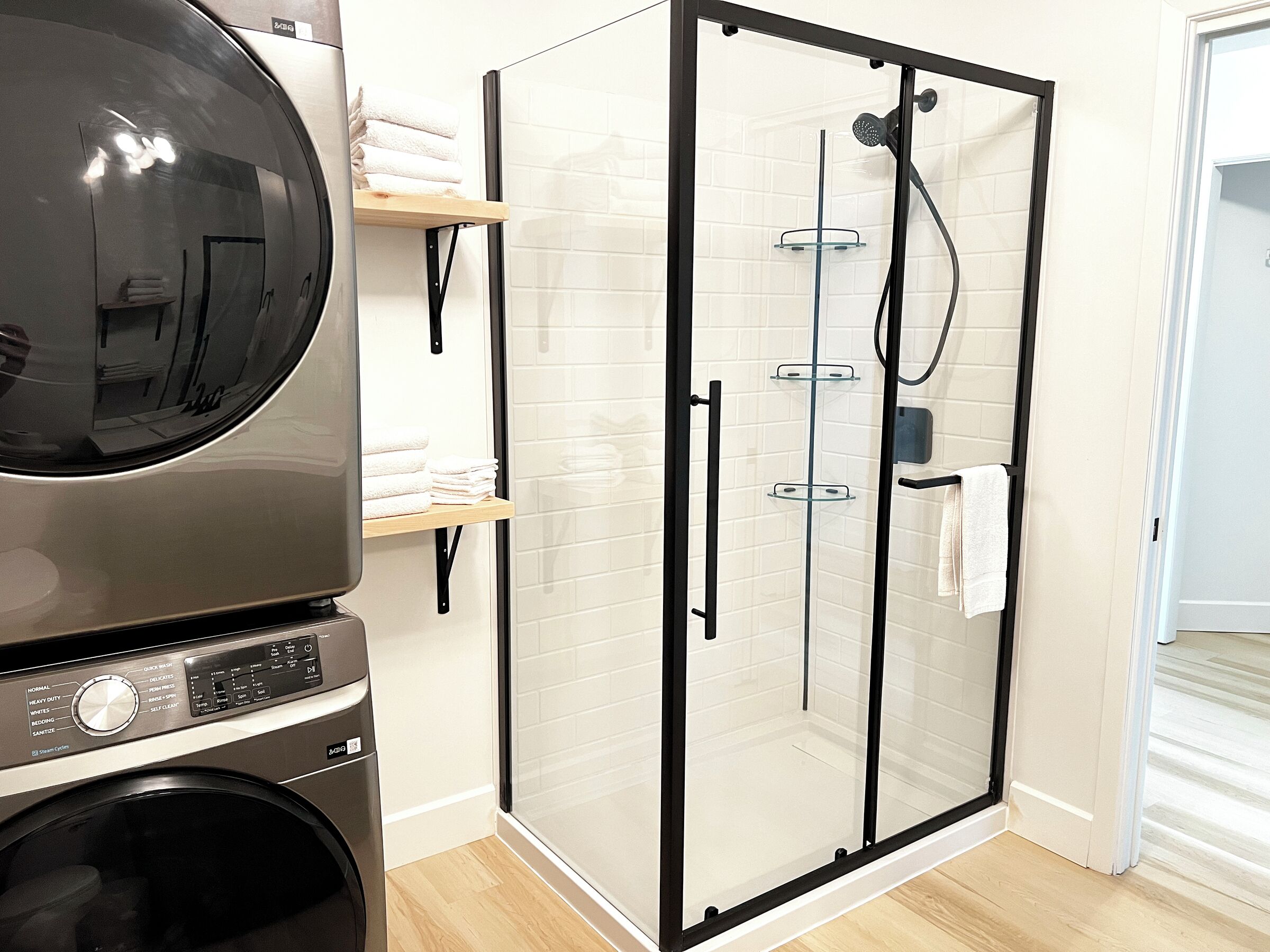 A laundry area with a washing machine, a glass-enclosed shower, and a towel rack.