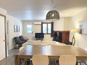 Un comedor con una mesa y sillas de madera, un televisor, una chimenea y una lámpara en el techo.