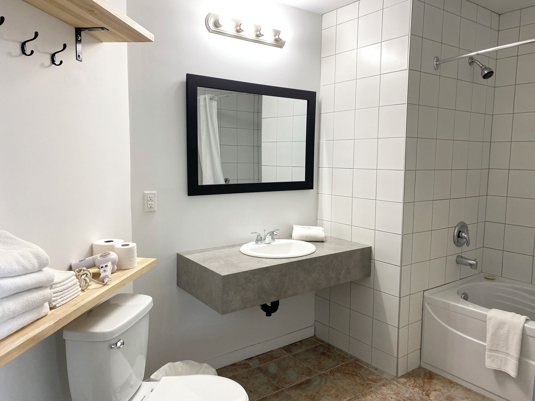Casa de banho moderna com lavatório branco, espelho e chuveiro. Há toalhas e artigos de higiene pessoal no balcão.