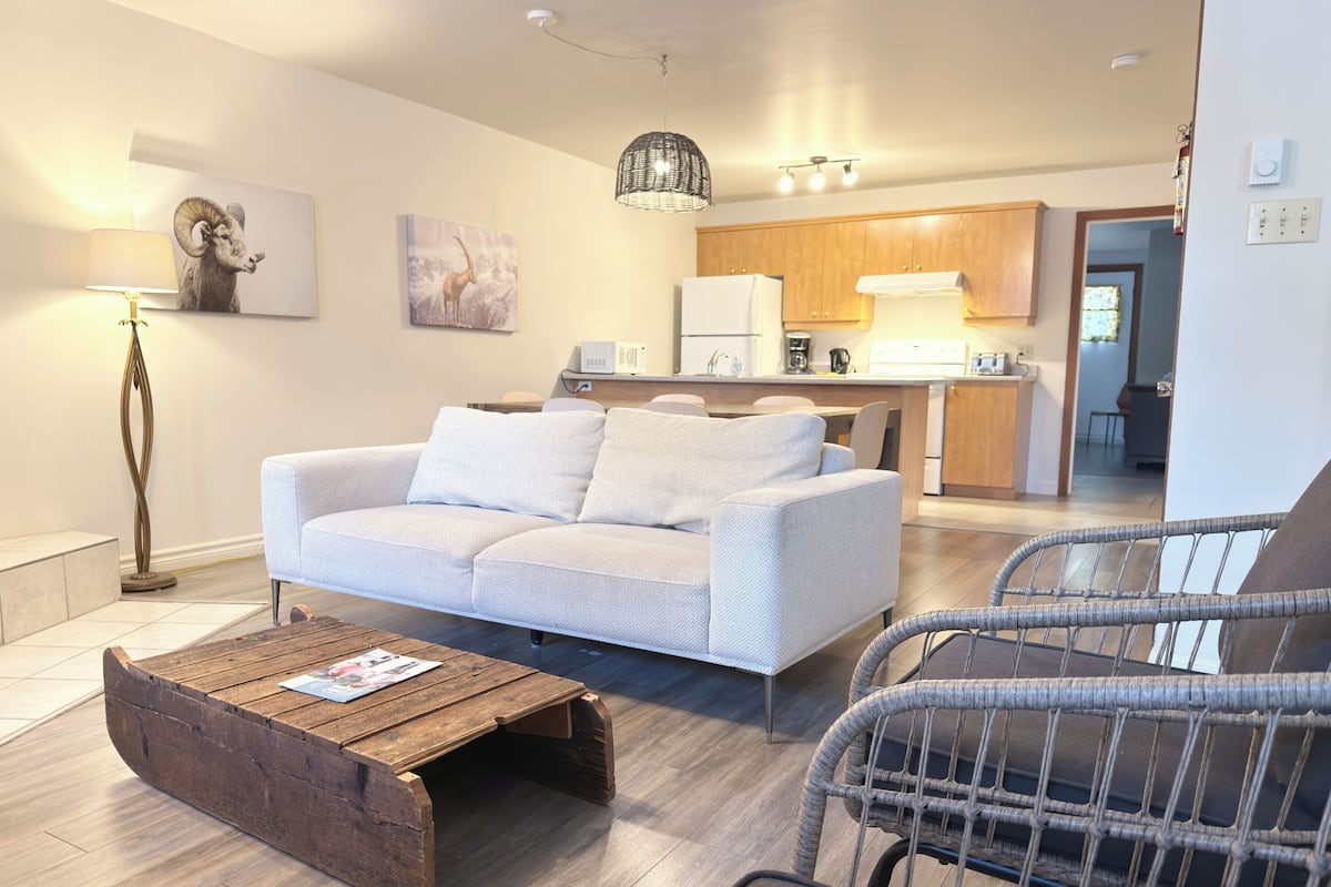 A modern living room with a sofa, a coffee table, a chair, and a kitchen in the background.