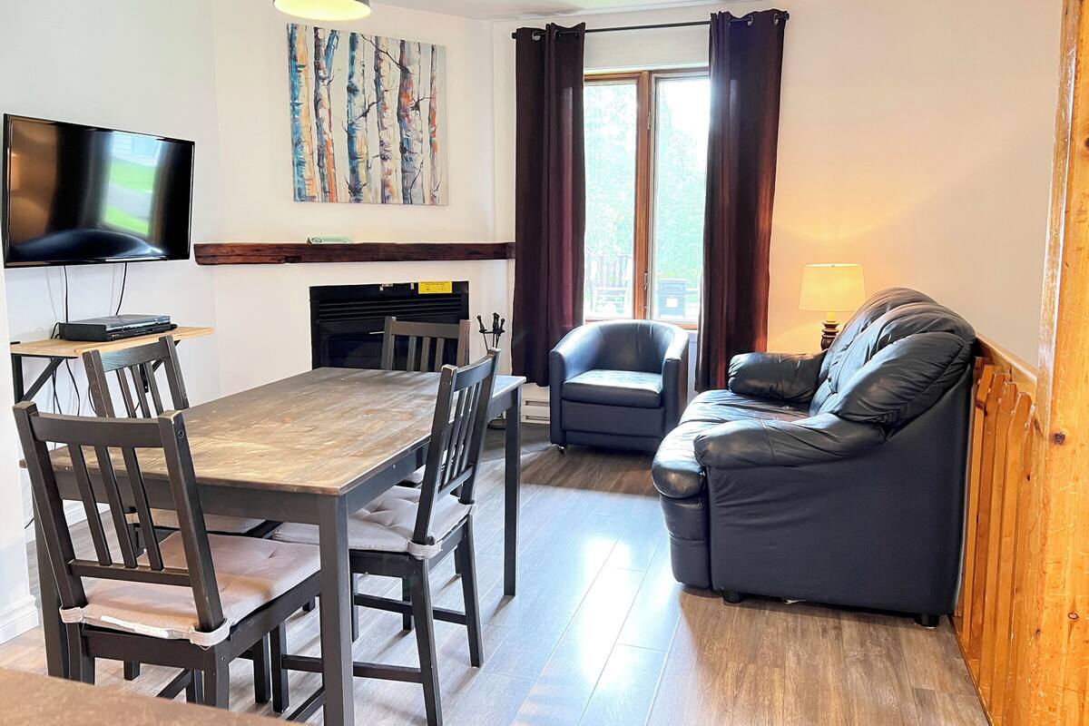 A modern living room with a dining table, chairs, a sofa, a TV, and a window with curtains.