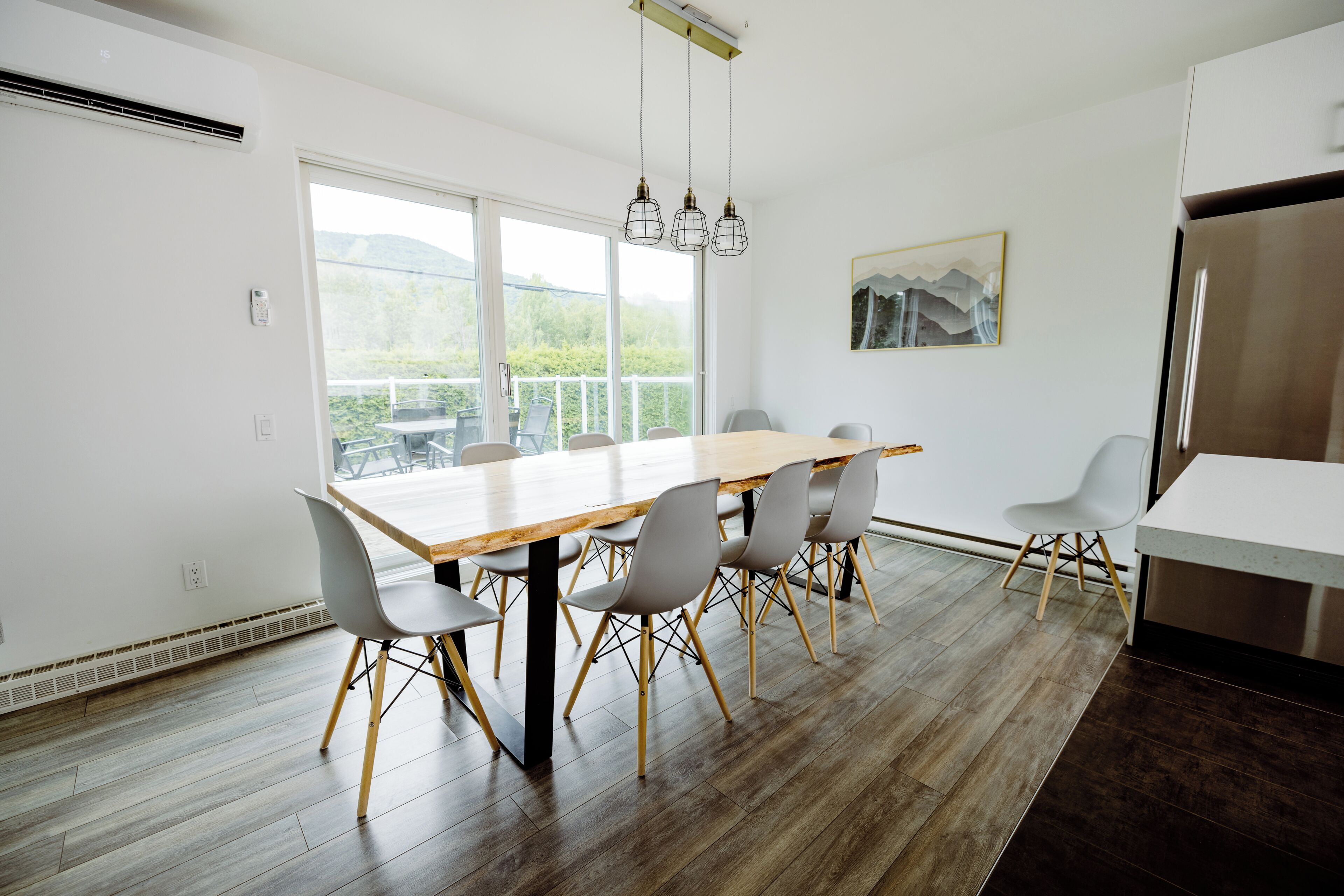 Una cocina moderna con una mesa de comedor de madera, sillas grises, un refrigerador de acero inoxidable y un ventanal que ofrece vistas al verdor.