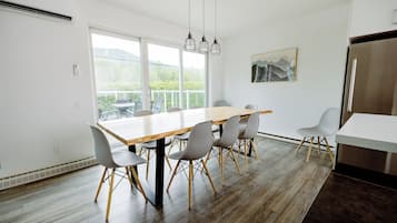 Una cocina moderna con una mesa de comedor de madera, sillas grises, un refrigerador de acero inoxidable y un ventanal que ofrece vistas al verdor.