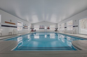 Una amplia piscina cubierta con agua cristalina, rodeada de paredes blancas y grandes ventanales.