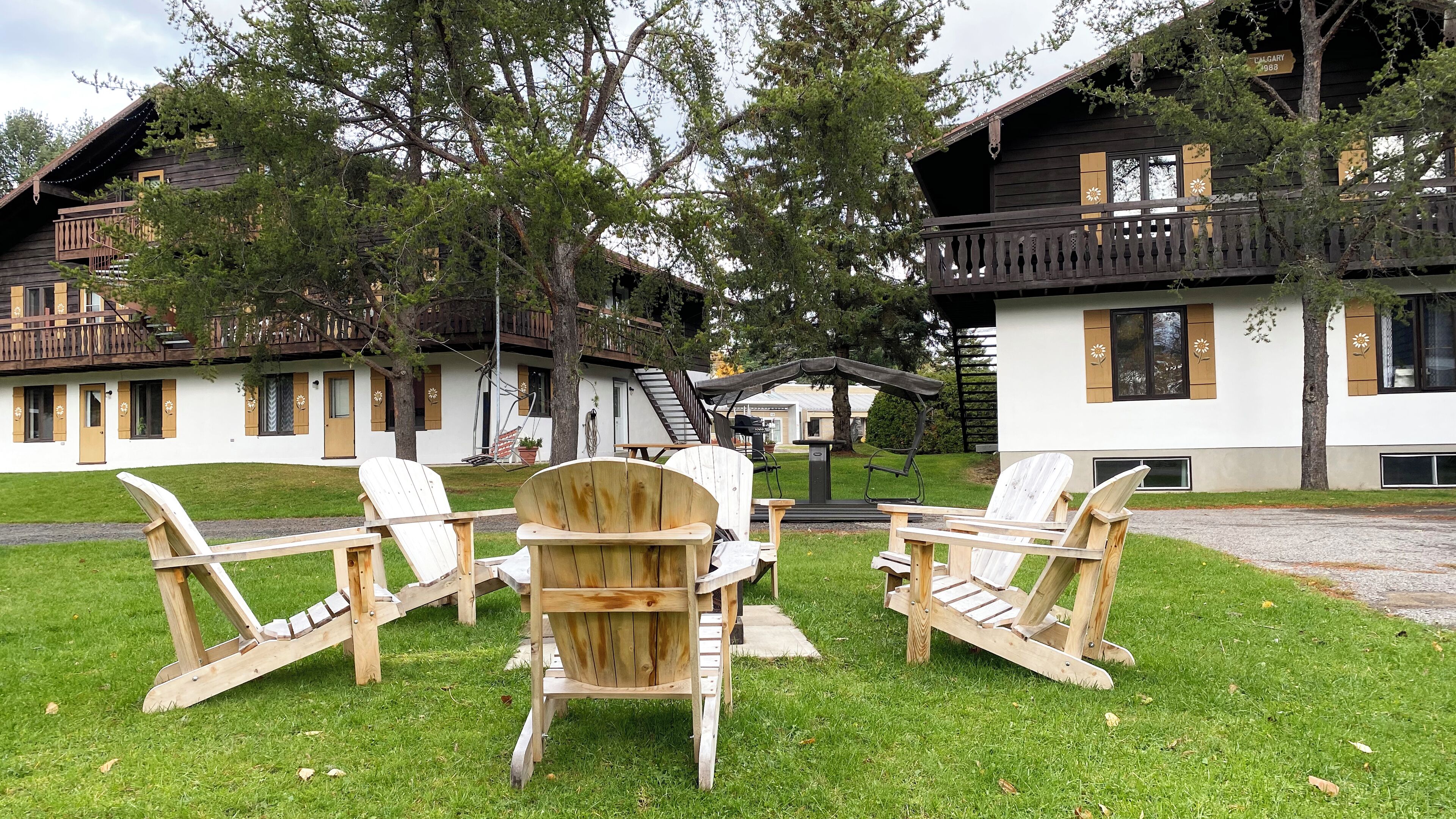 A chalet-style building with a wooden deck, outdoor seating, and a staircase leading to a balcony.
