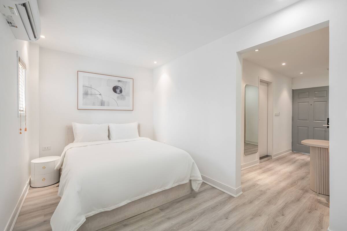 A modern bedroom with a large bed, a bedside table, a framed artwork on the wall, and a view into the adjacent bathroom.