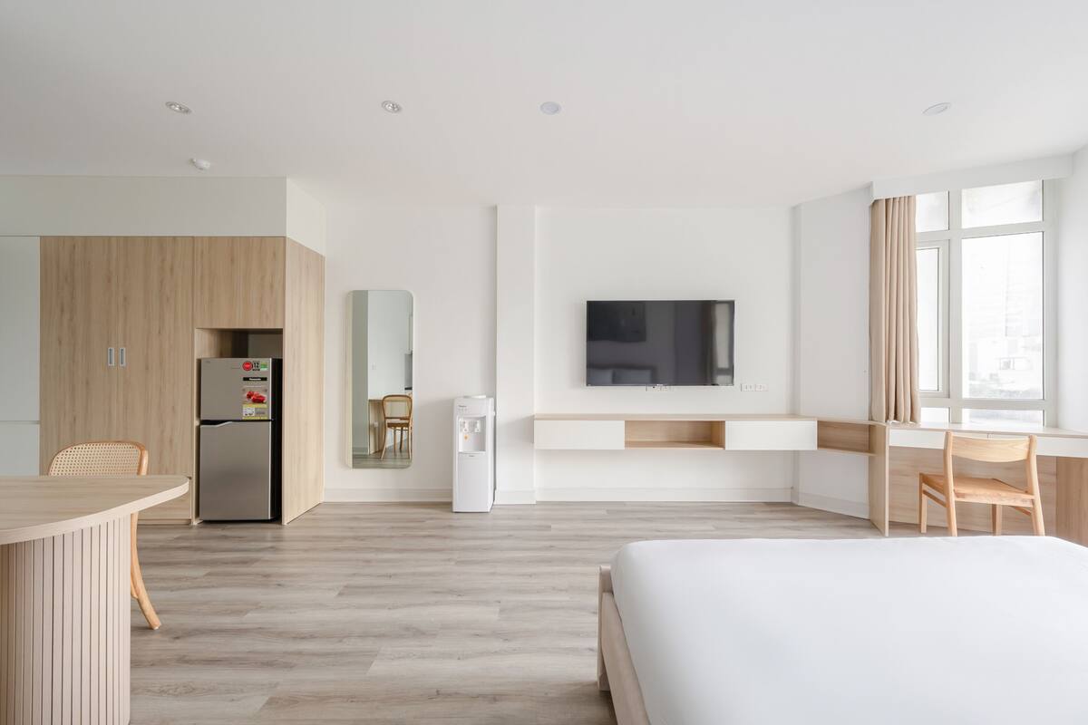 A modern hotel room with a kitchenette, a bed, a TV, and a large window.