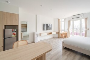 Hotelkamer met een bed, bureau, stoel, koelkast, televisie en een balkon met gordijnen.