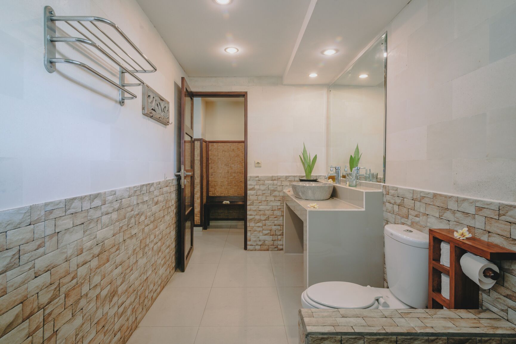 A bathroom with a toilet, sink, and mirror. There is a towel rack on the wall and a plant on the sink counter.