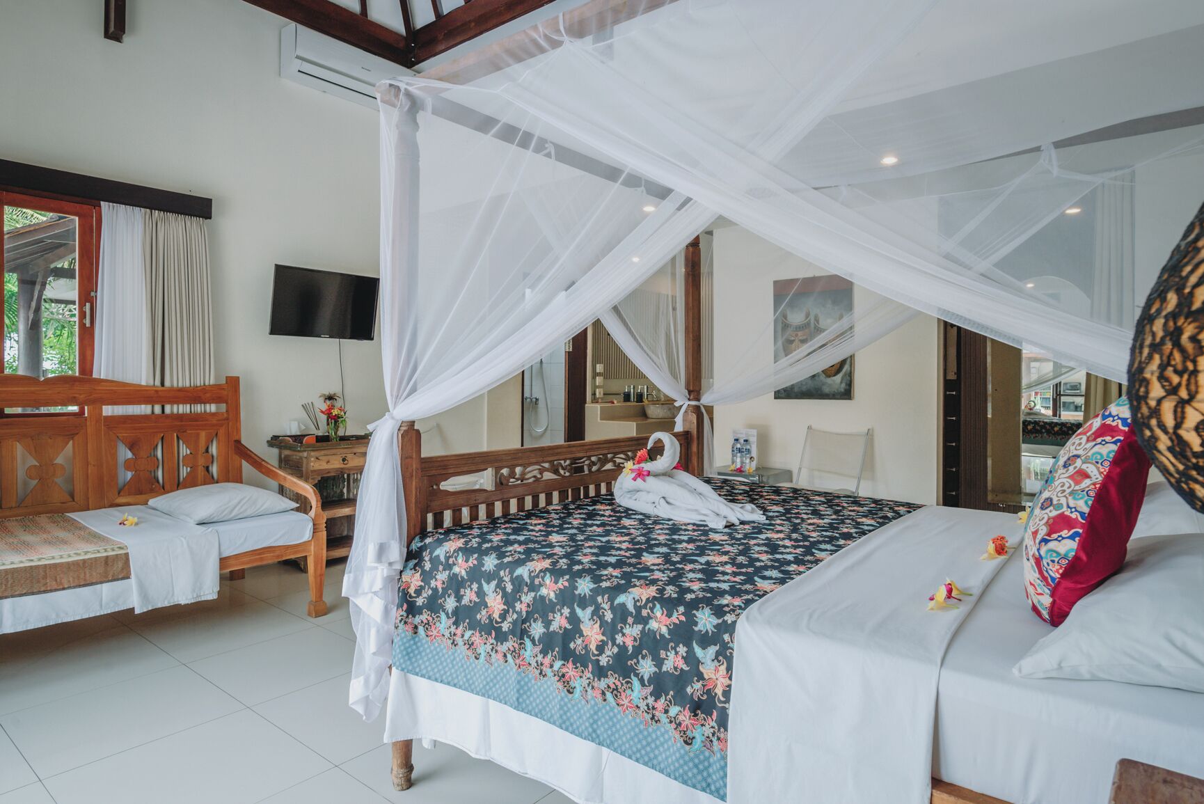 A bedroom with a bed under a canopy, a wooden bench, a small table with toiletries, and a TV on the wall.