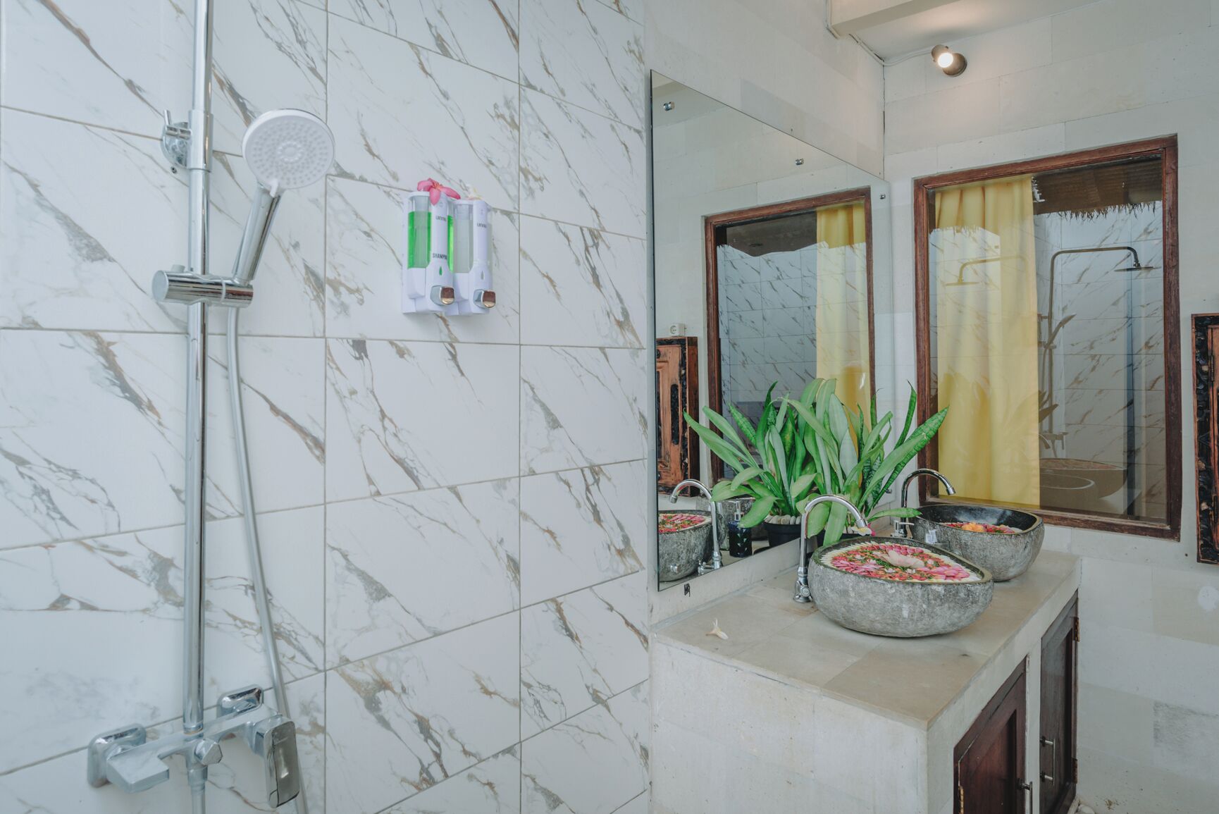 A bathroom with a marble floor, a shower, a sink with a flower vase, and a mirror.