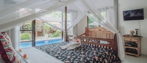 Un dormitorio con cama, mesita de noche, televisor y vistas a una piscina y jardín.