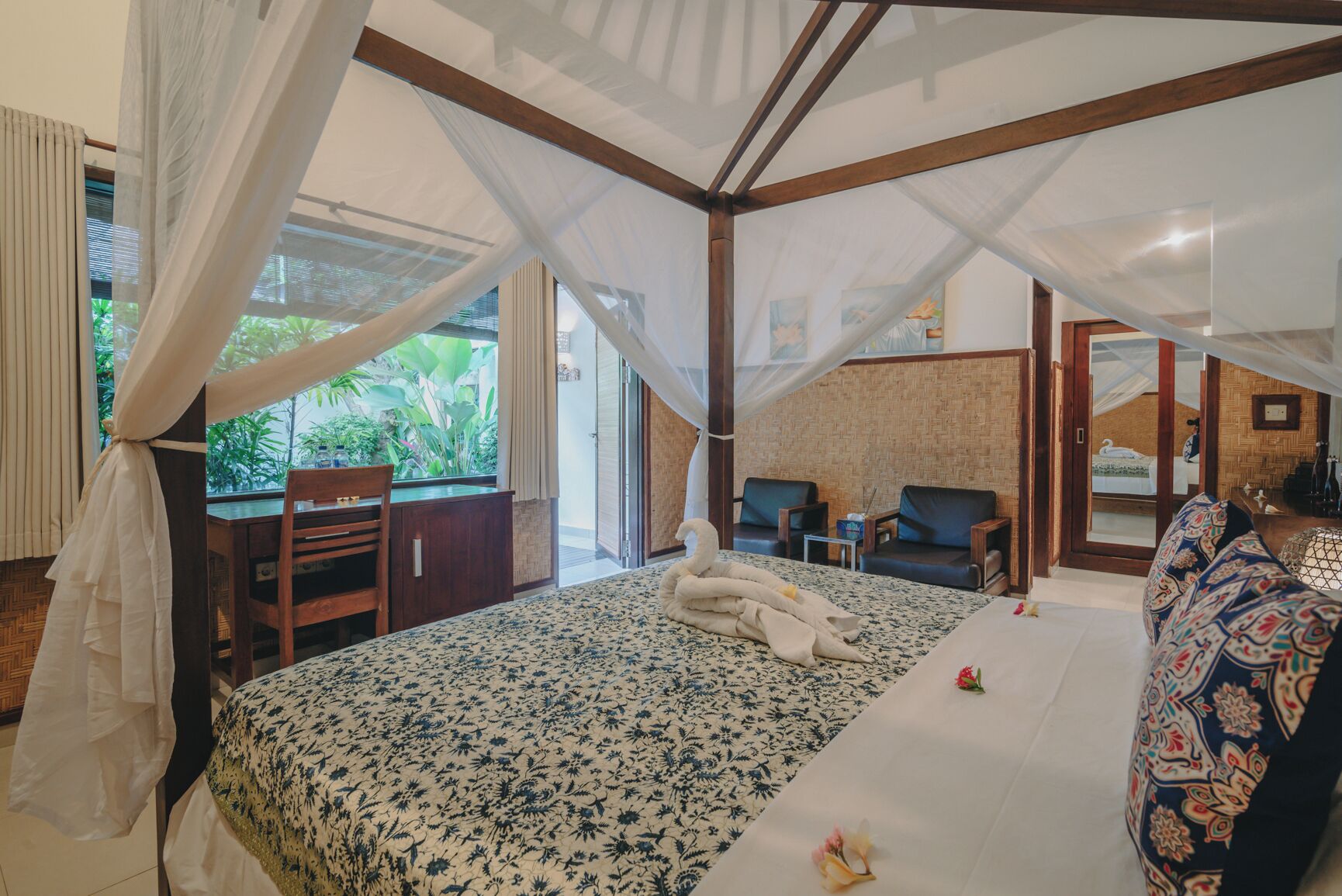 Un dormitorio con cama, escritorio y silla. Se ve una ventana con cortinas y vistas a vegetación al exterior.
