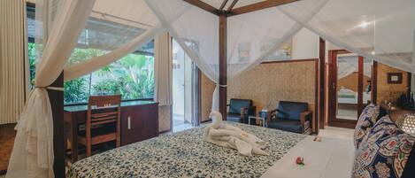 Un dormitorio con cama, escritorio y silla. Se ve una ventana con cortinas y vistas a vegetación al exterior.
