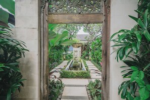A garden pathway leading to a central fountain, surrounded by lush greenery and a decorative wooden archway.