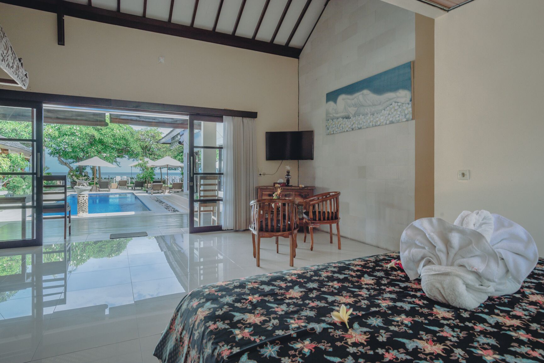A hotel room with a bed, a desk, a chair, a TV, and a view of an outdoor swimming pool.