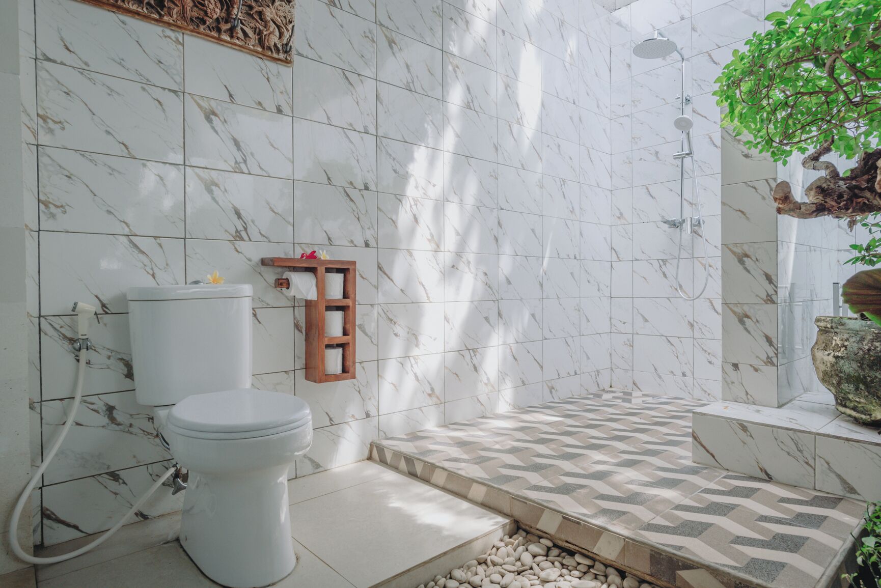 A bathroom with a toilet, marble tiles, a shower, and a small shelf with a plant.