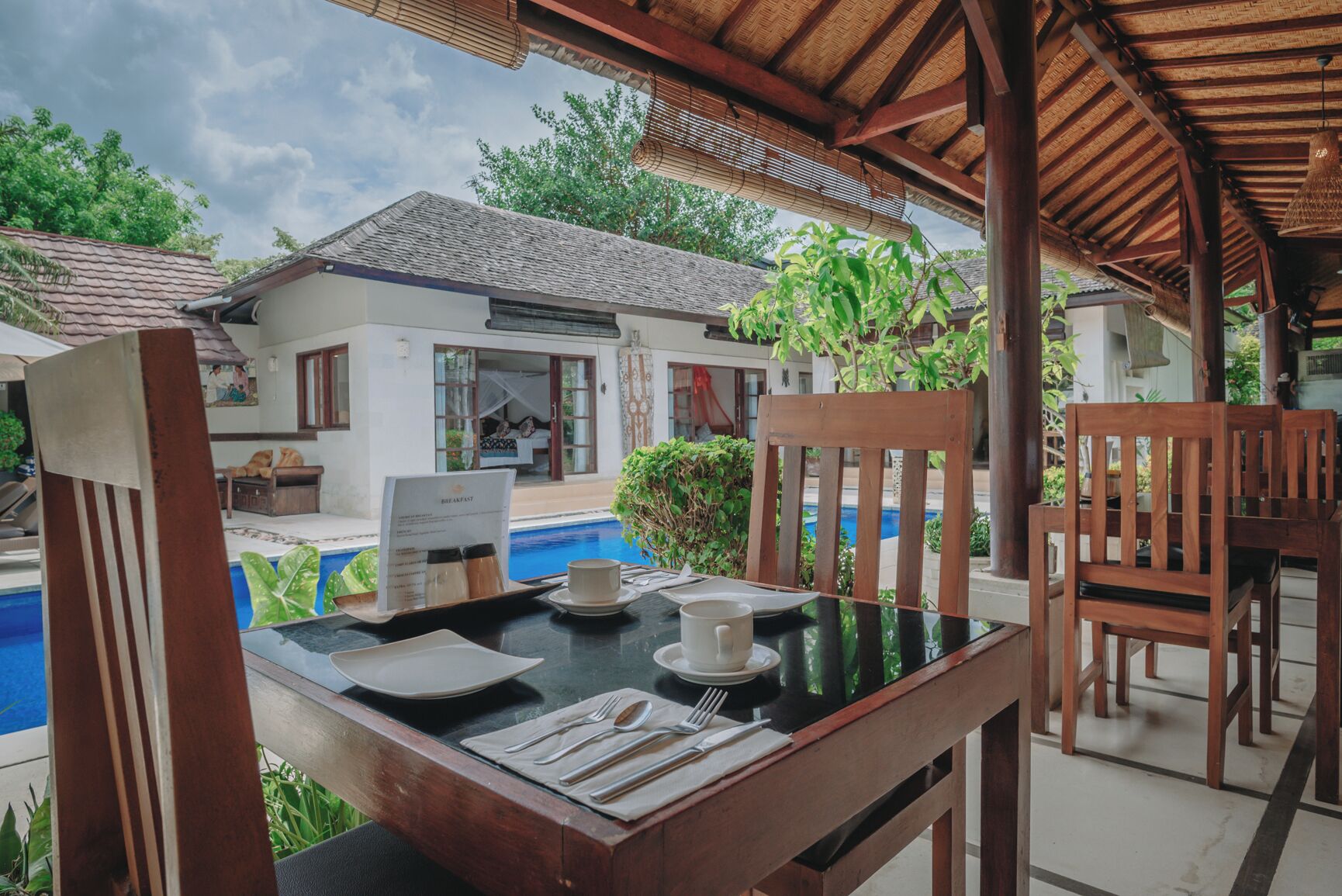 Un comedor con una mesa dispuesta para el desayuno, con vista a una piscina y una casa con tejado de tejas.