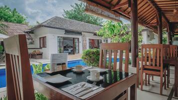 Un comedor con una mesa dispuesta para el desayuno, con vista a una piscina y una casa con tejado de tejas.