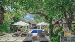 Uma área junto à piscina com espreguiçadeiras, guarda-sóis e piscina.