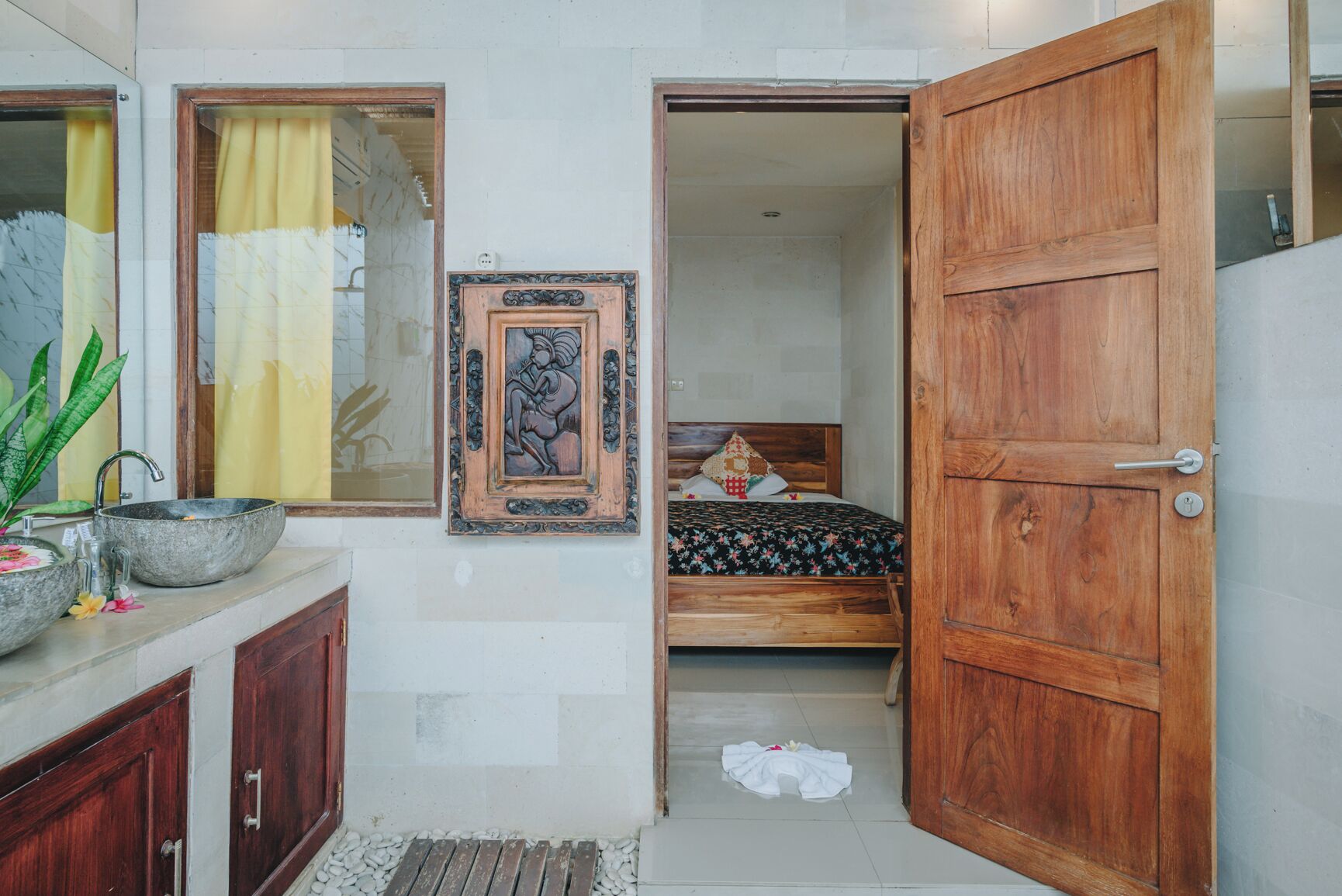 Un baño con puerta de madera, un lavabo con un cuenco decorativo y una obra de arte enmarcada en la pared.