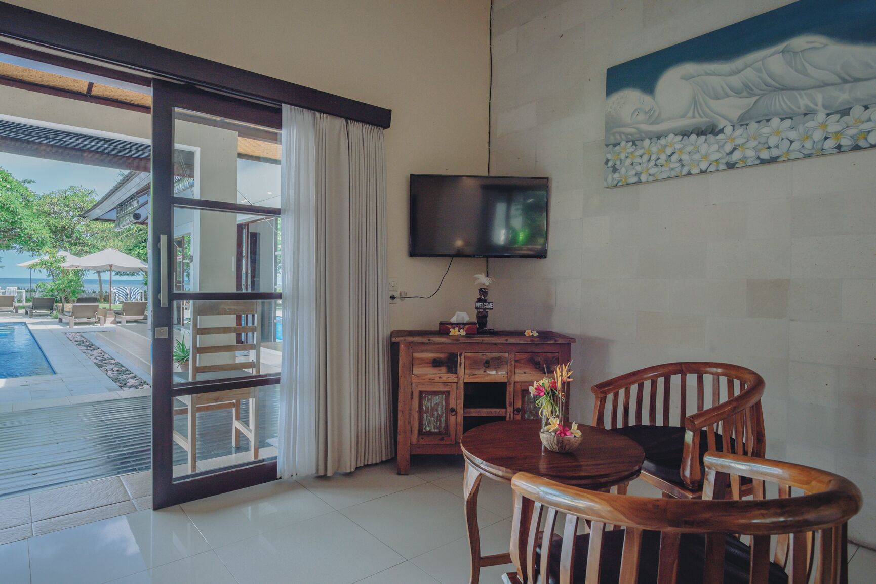 Una habitación con escritorio de madera, televisor y vistas a una piscina y zona de estar al aire libre.
