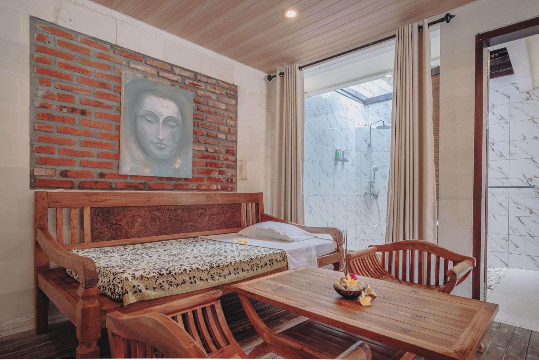 Een gezellige kamer met een houten bed, een eettafel met een schaal fruit en uitzicht op een badkamer met douche.