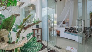 Quarto moderno com porta de vidro, cama com dossel e planta em vaso.