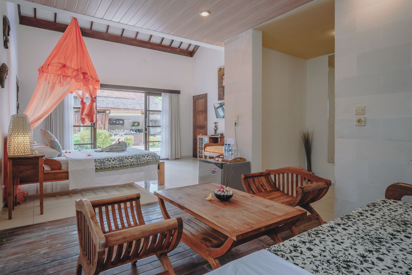 A spacious room with a wooden dining table, two wooden chairs, a bed with a canopy, and a view of the outside.