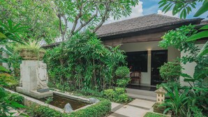 Uma casa tradicional com telhado de telhas, rodeada por vegetação exuberante e um pequeno lago.