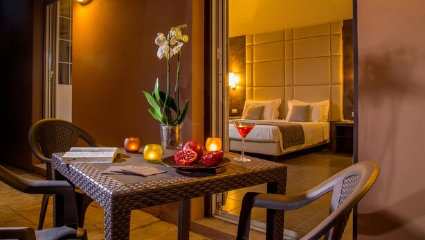 A hotel room with a bed, a dining table with candles, a potted plant, and a martini glass. - Hearth Hotel (Rome)