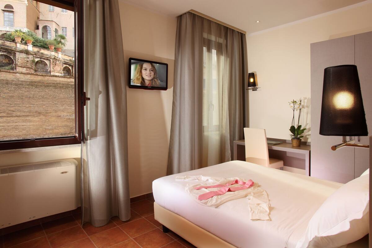 A hotel room with a bed, a desk, a chair, a TV, and a window with curtains.