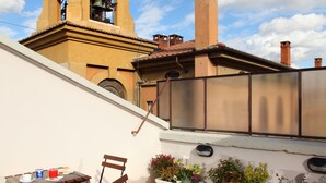 An outdoor patio with a table and chairs, a bell tower in the background, and a view of a building with a chimney. - Hearth Hotel (Rome)