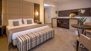 A modern hotel room with a large bed, a bedside table, a bench, a dining area with a table and chairs, and a kitchen area with a counter and decorative items. - Hearth Hotel (Rome)
